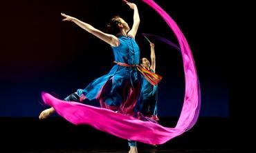 A dancer with a very long. pink piece of fabric that she is twirling